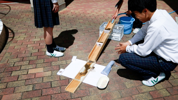 賢明学院高等学校の生徒が傾斜のある木材にホースで水を流すようす